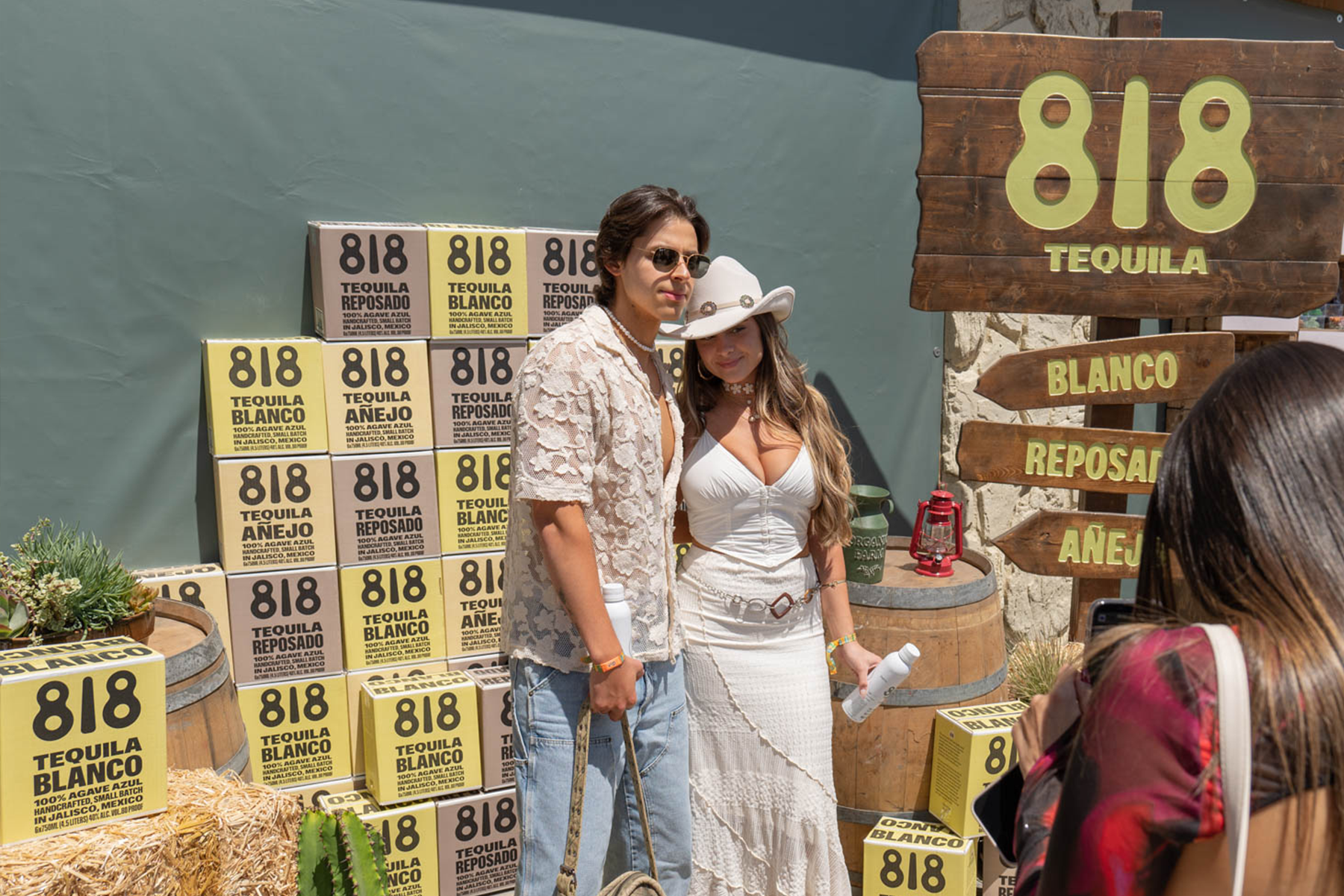 Two people dressed in western clothing in front of a stack of 818 Tequila boxes.