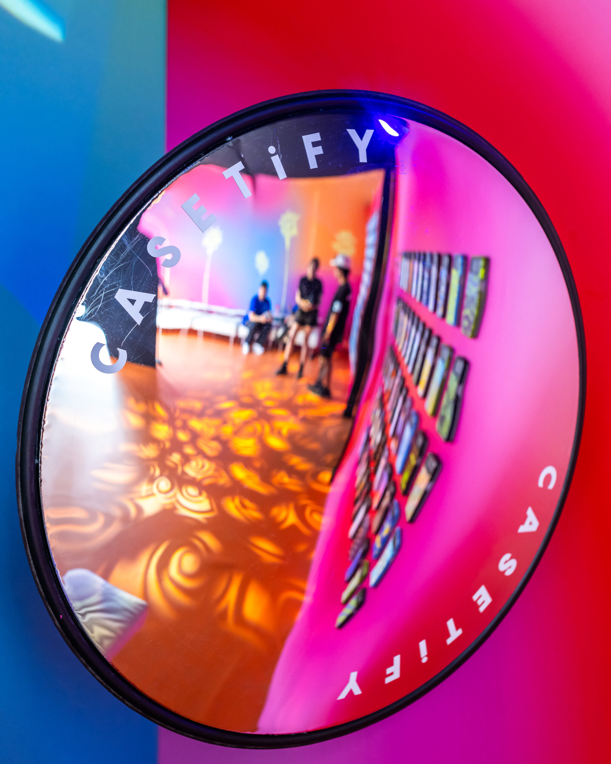 A mirror with the reflection showing a product display and people enjoying the lounge.