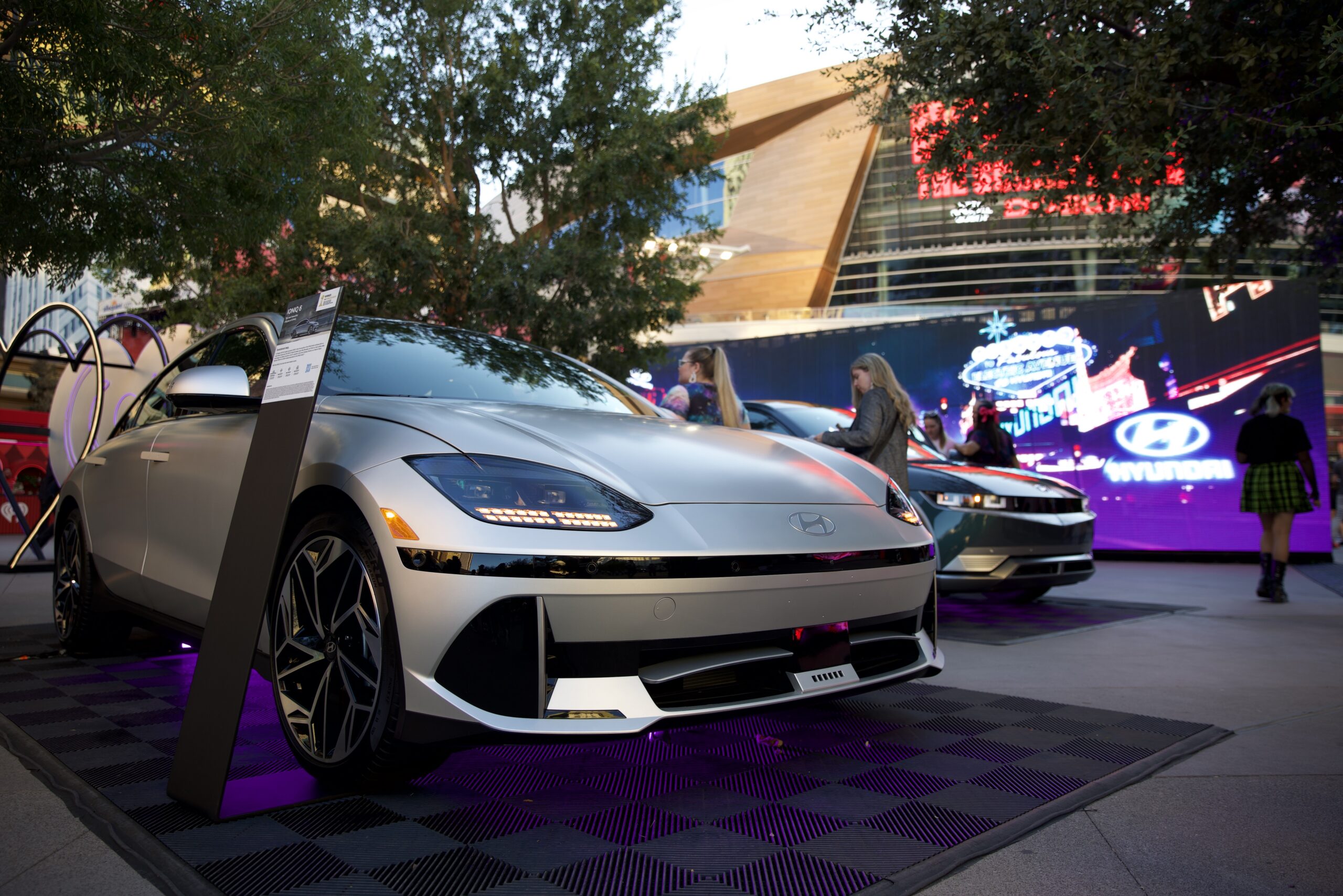 Cars on display in front of a screen showing a cruise down a cyber Las Vegas.