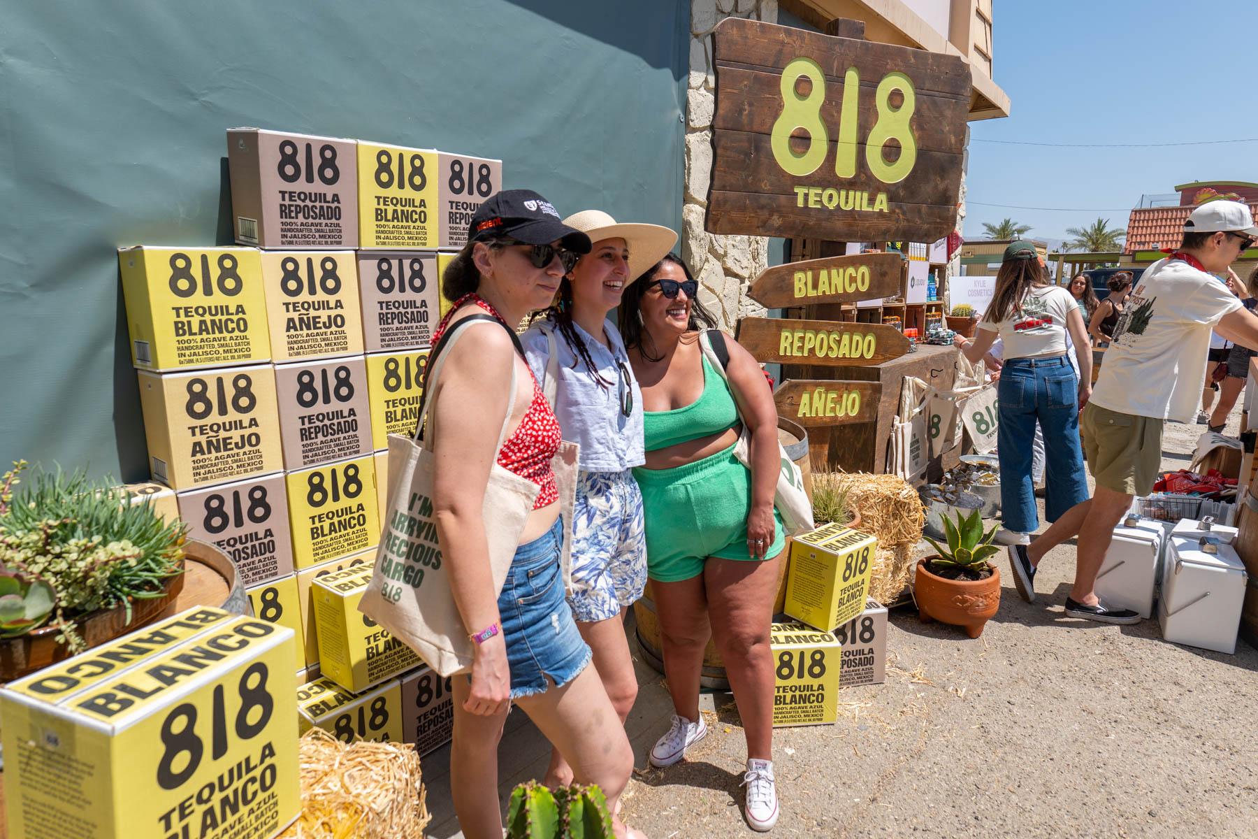 Three people posing in front of a stack of 818 Tequila Boxes at the 818 Tequila Coachella Pop-Up.