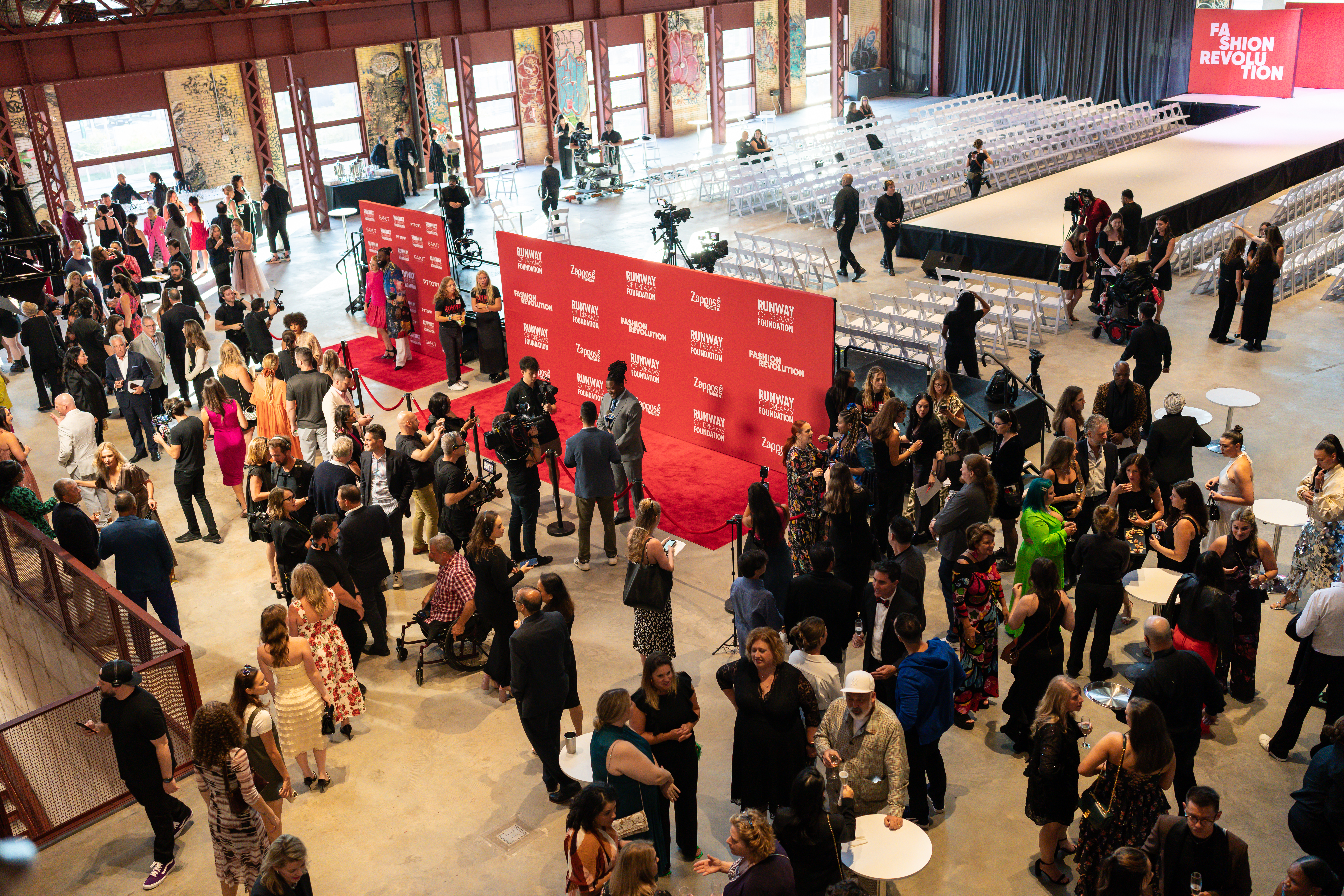 A birds-eye view of models, staff, and guests on the red carpet in front of the stage.