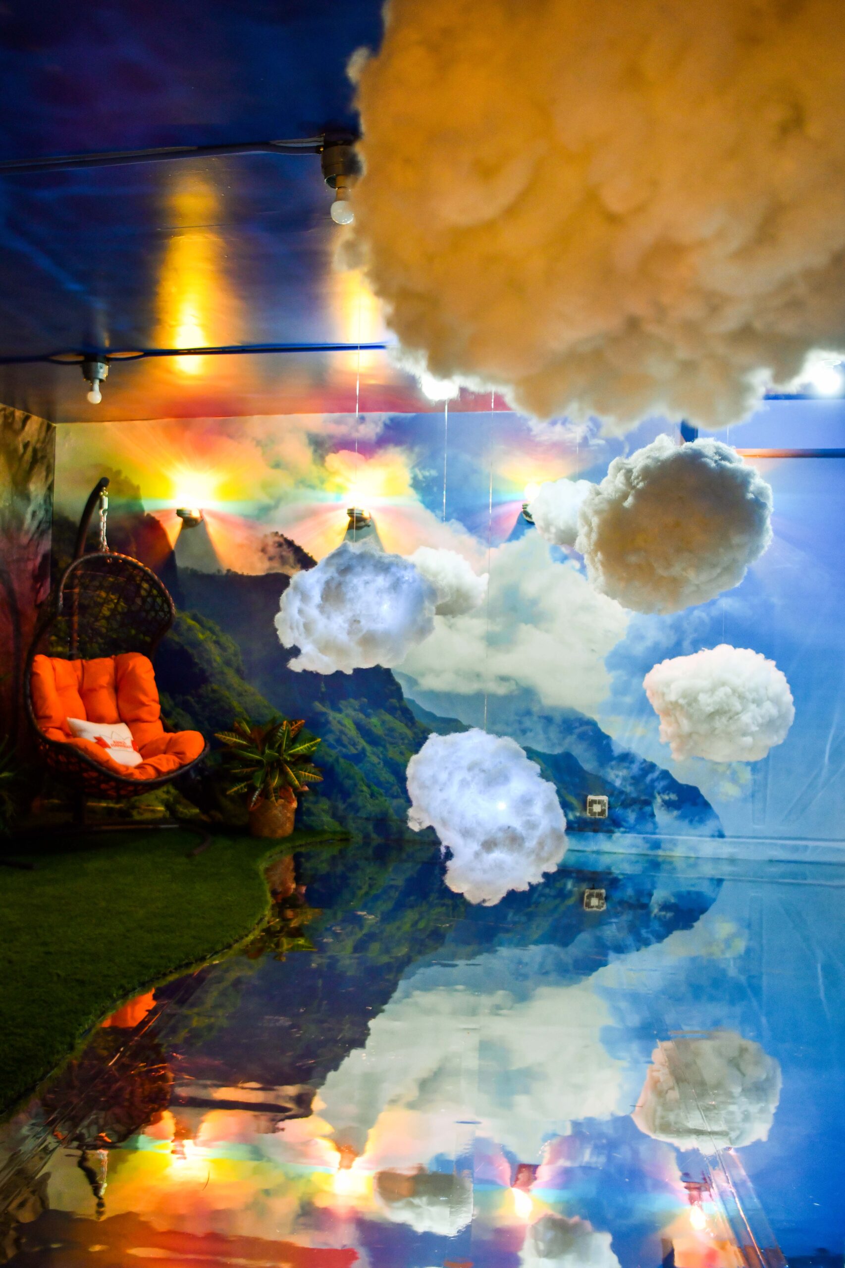 A sunset photo backdrop with a lounge chair, mirror floor, and dimensional clouds.