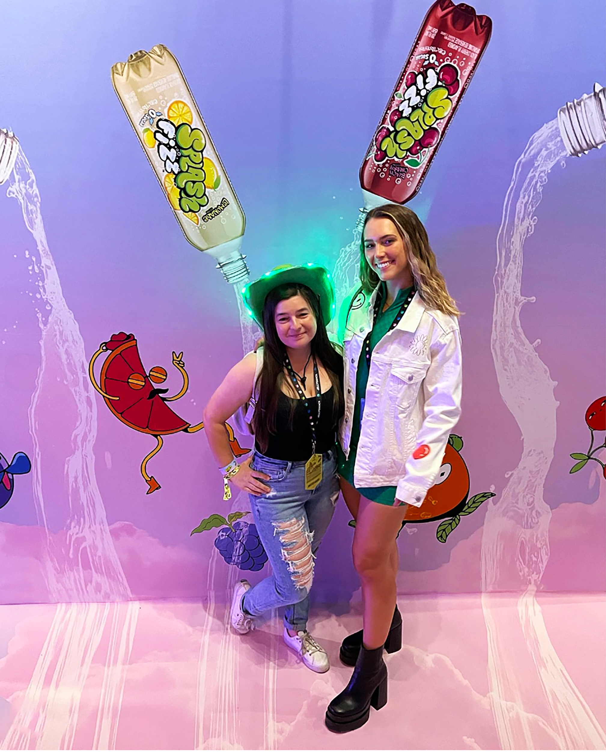 Two friends posing in front of a backdrop of fruit characters and cascading Splash water.